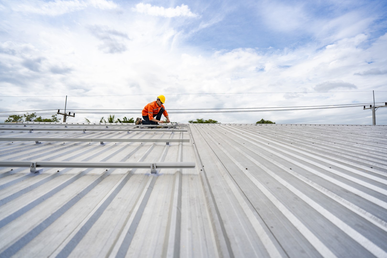 Technician in safety uniform and helmet kneeling on a rooftop, using a drill for precise installation work. A scene highlighting safety, professionalism, and technical expertise in construction.